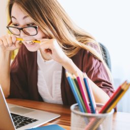 woman biting on pencil looking at computer
