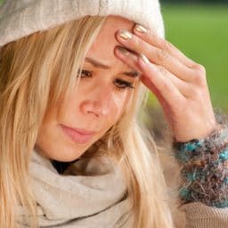 woman with a red nose putting her hand up to her head in pain