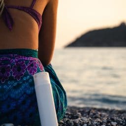 woman sitting on a shaded beach with a bottle of sunscreen