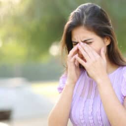 Woman with allergies suffering from a sinus headache in a park.