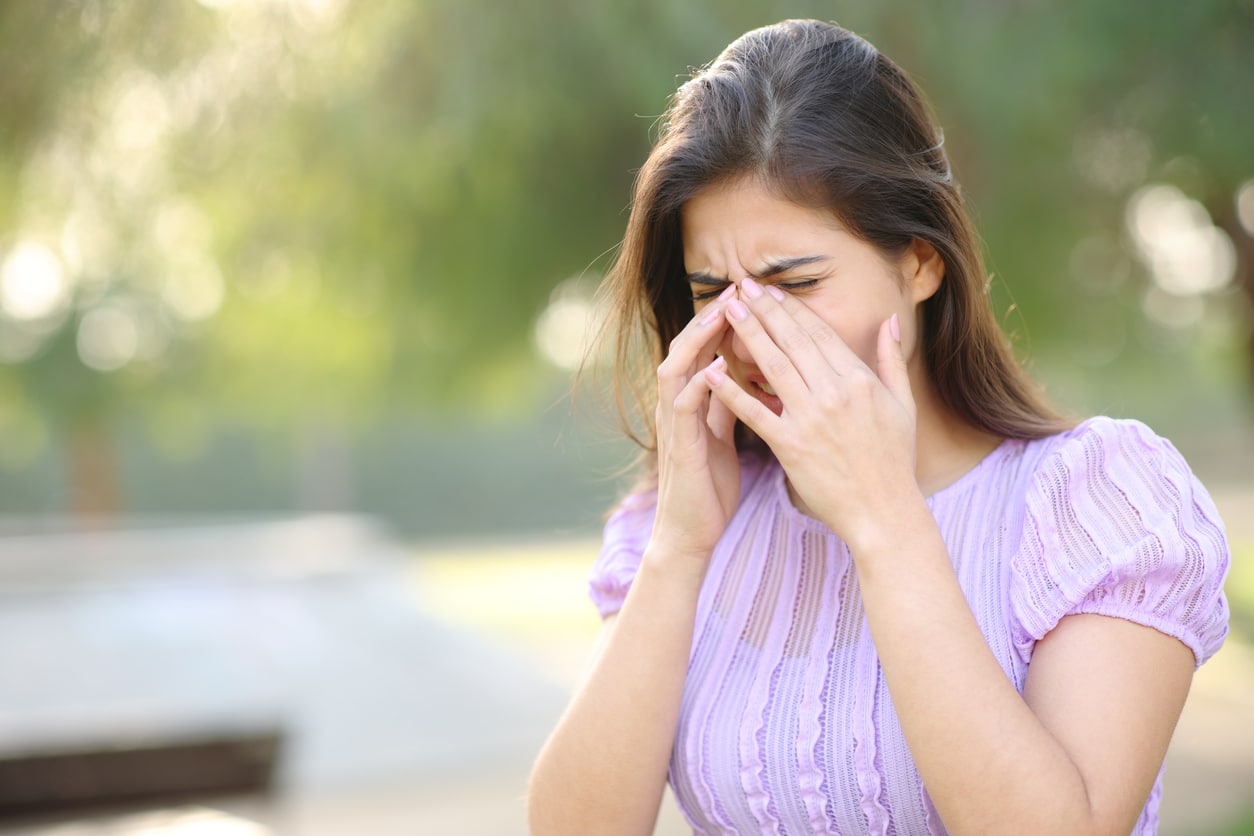 Woman with allergies suffering from a sinus headache in a park.