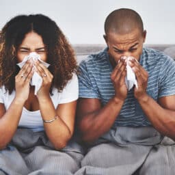 A couple blowing their noses on the couch.
