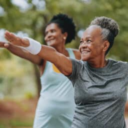 Two women doing warrior pose yoga in a park